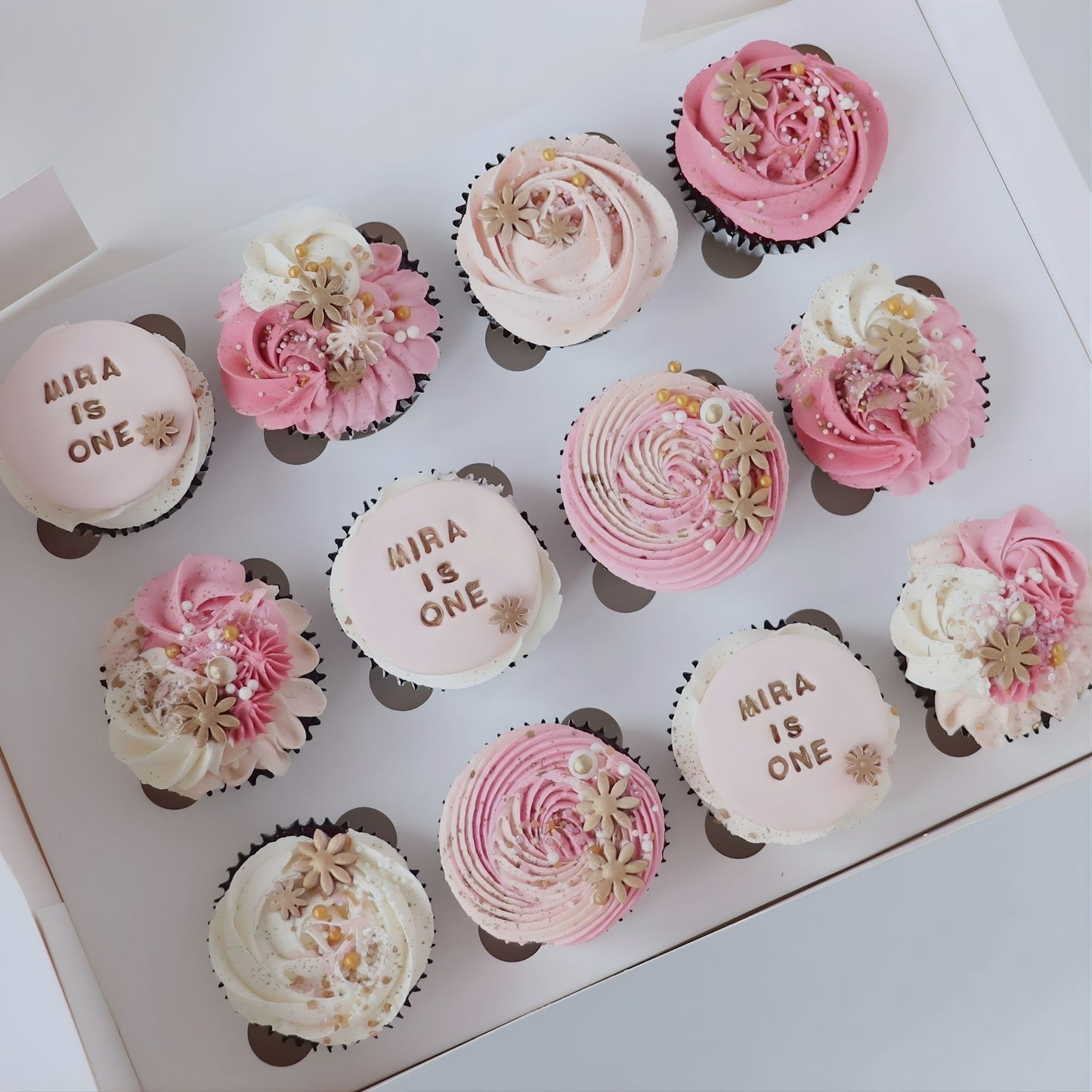 Pink cupcakes decorated with delicate piping, flowers and sugar pearls. Featuring 3 x matching custom name and age plaques.