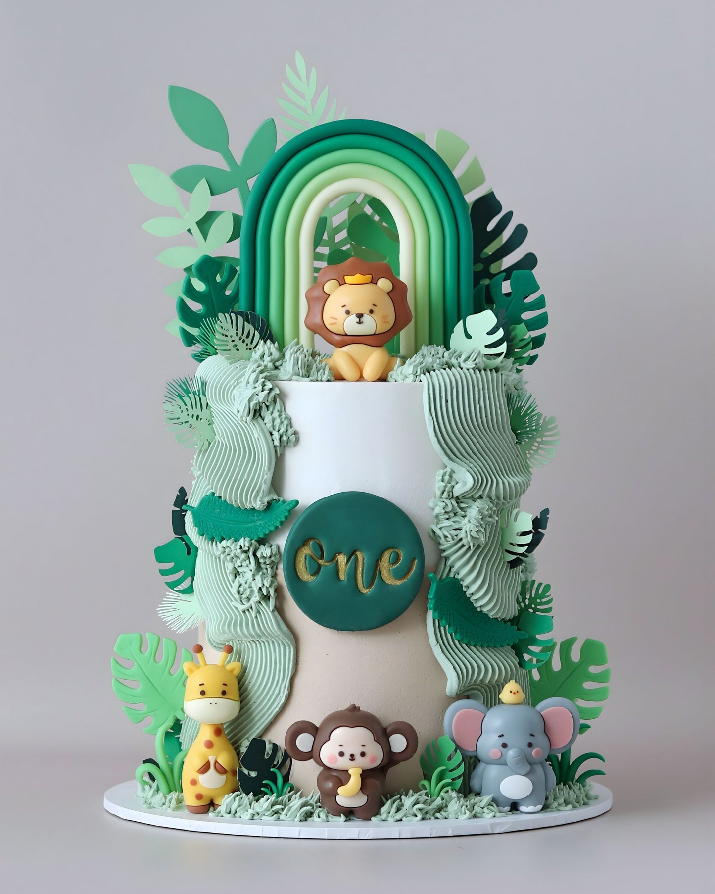 Green and white jungle animal celebration cake with ferns and rainbow topper.