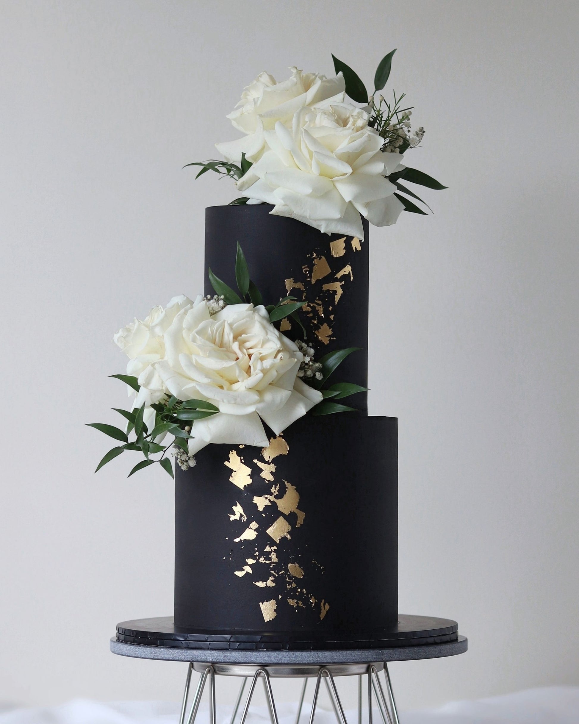 A modern wedding cake in black and gold. Featuring delicate all-around stencil overlay, fresh flowers, and gold accents. 