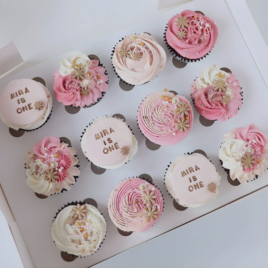 Pink cupcakes decorated with delicate piping, flowers and sugar pearls. Featuring 3 x matching custom name and age plaques. 