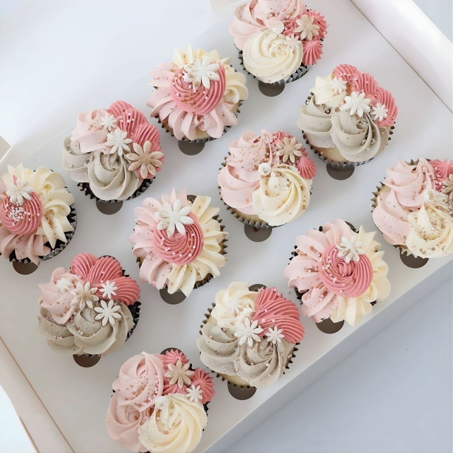 Pink and white cupcakes decorated with delicate piping, flowers, gold accents, and sugar pearls